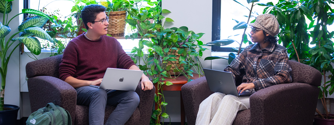 Two students sitting in chairs using laptops.