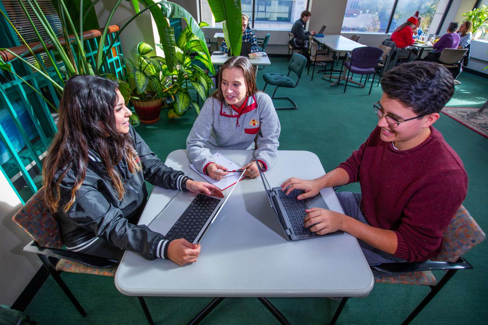 Students talking at a table and using laptops.